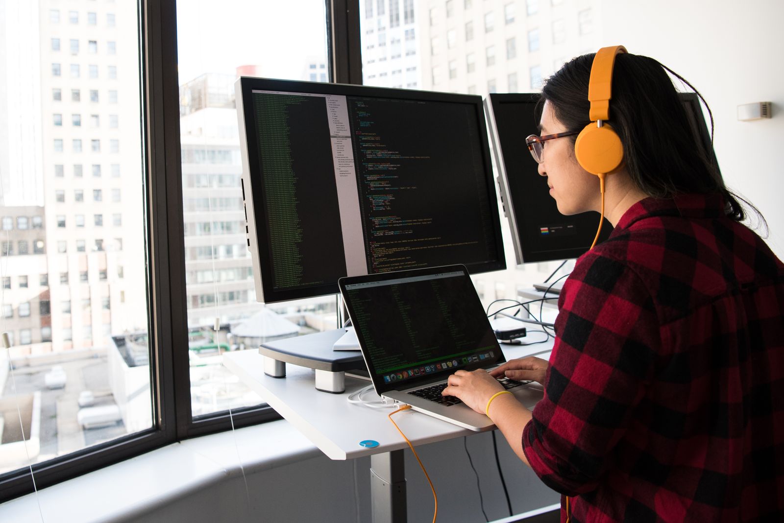 A developer wearing headphones working at a desk beside large office windows