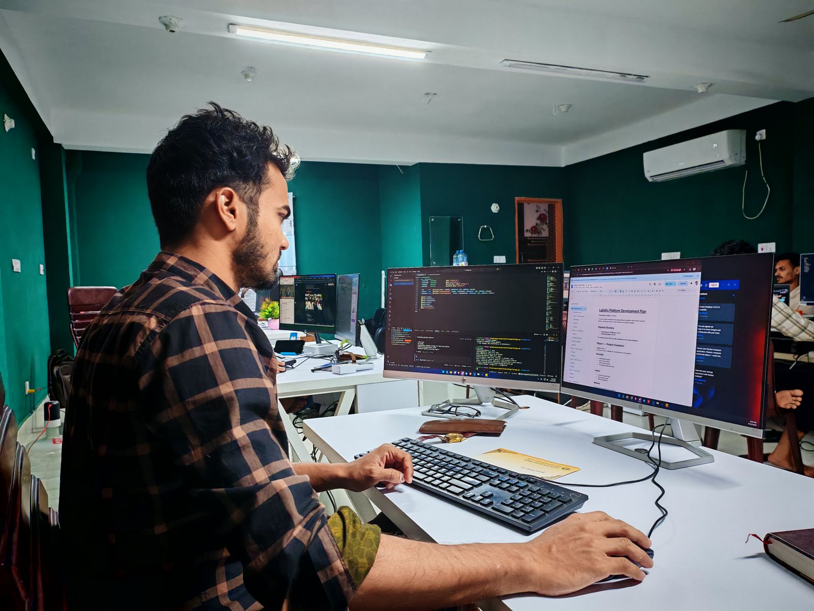 A software developer working at two monitors in a shared office